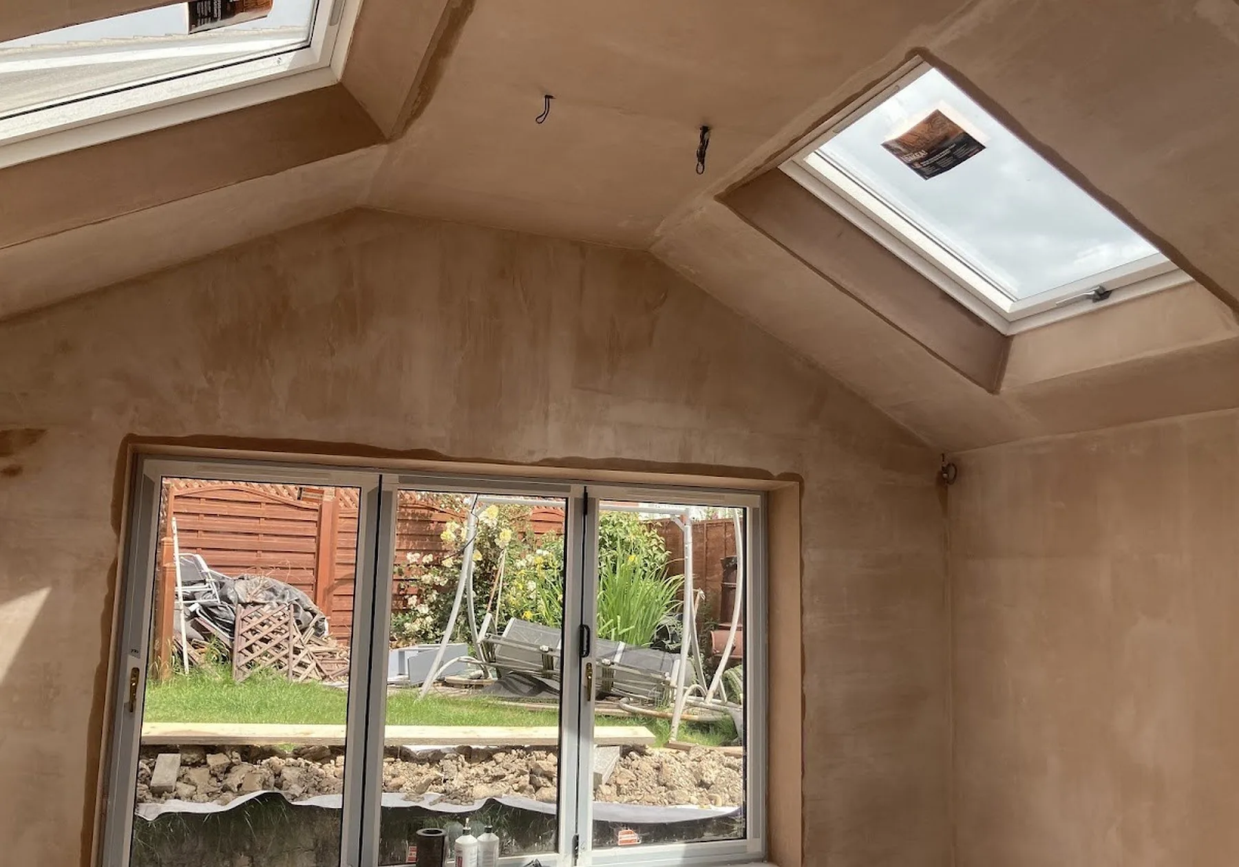Vaulted extension ceiling and walls freshly skimmed, with a Velux roof window and patio doors onto the garden